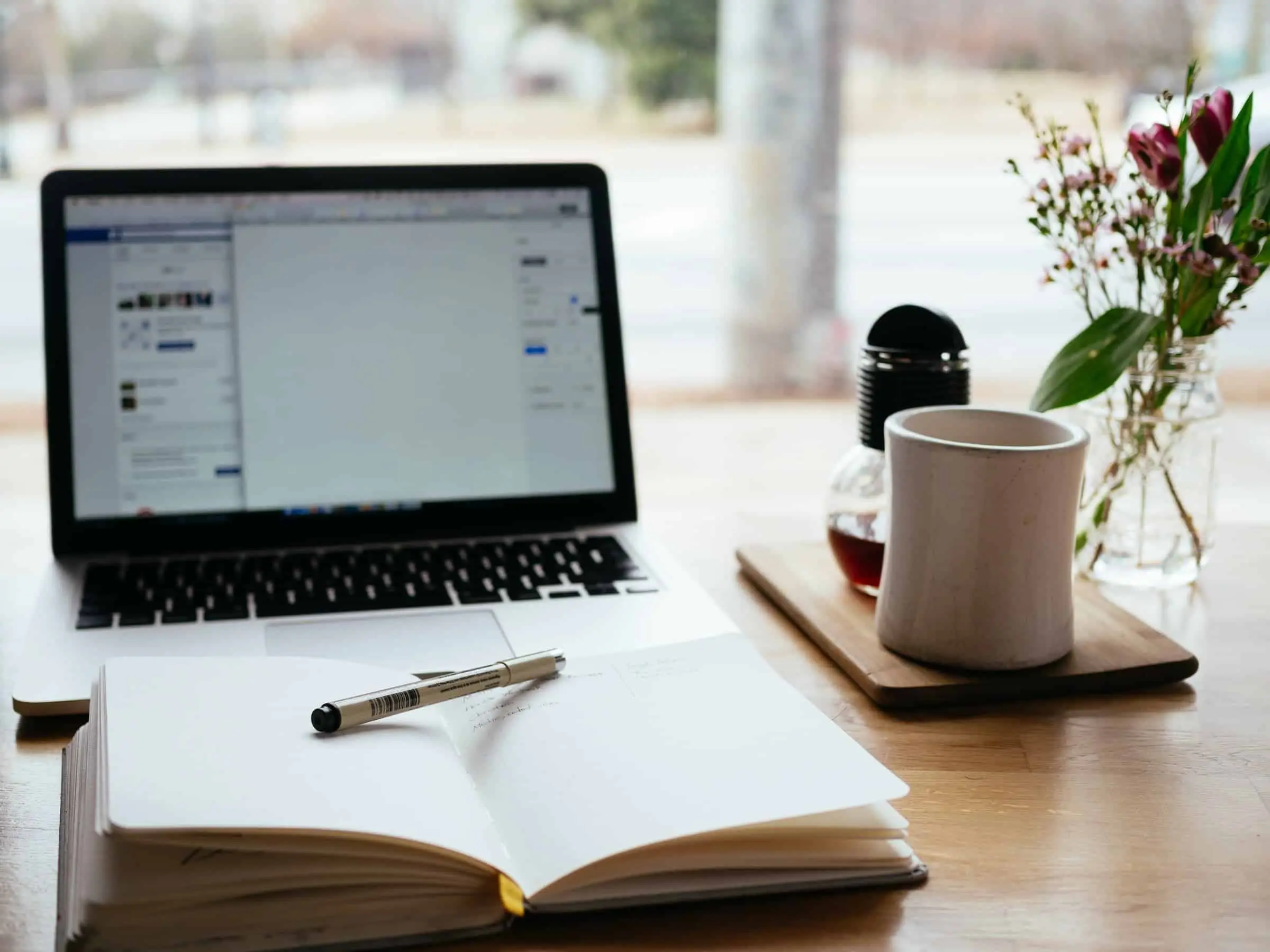 a laptop and a cup on a table with a book in front